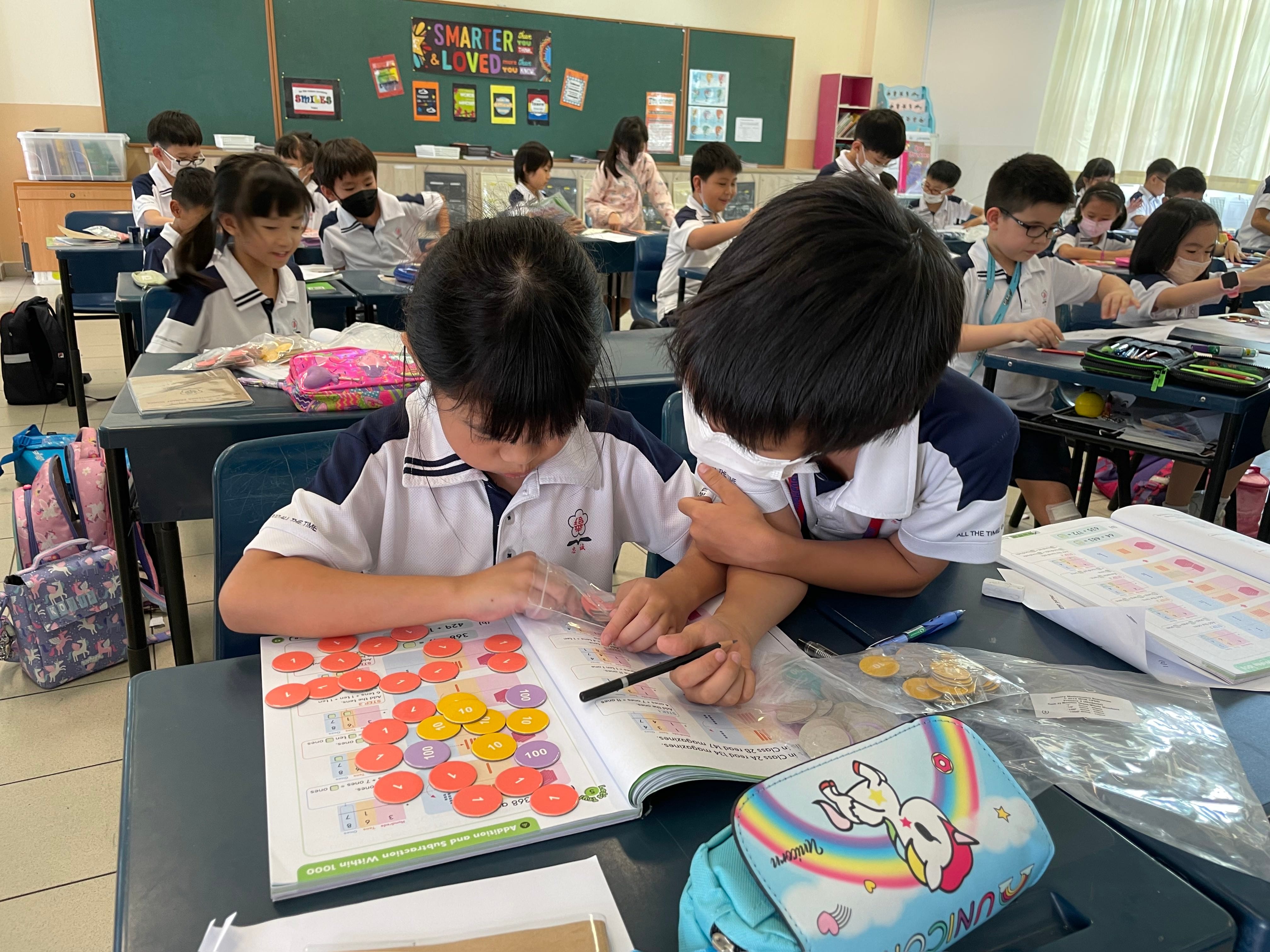 A pair of students using money discs to represent and check their understanding.